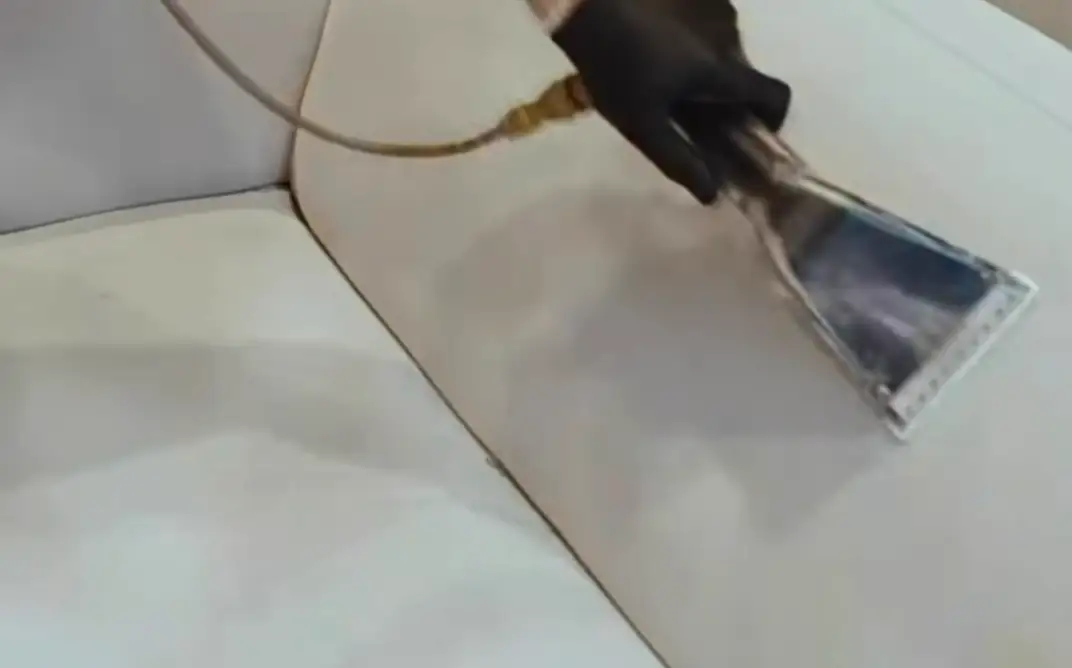 Clear extraction head pulling dirty water out of a light sofa