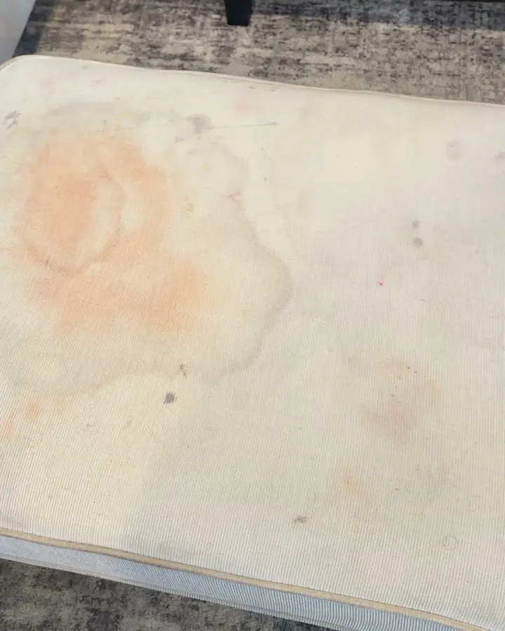 Cream ottoman before cleaning, with a large orange stain and scattered marks.