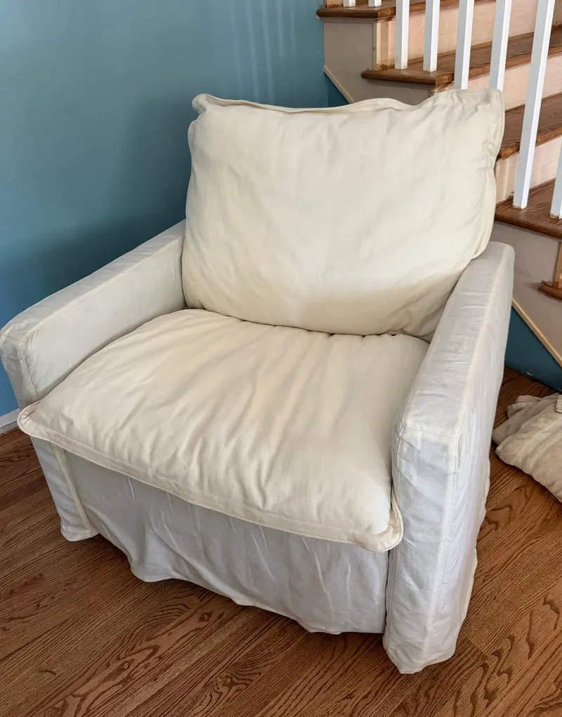 White slipcovered armchair after cleaning, next to a staircase and a blue wall.