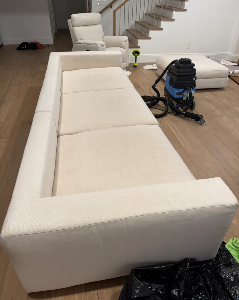 Long cream sofa after cleaning, with the extraction machine still set up behind it.