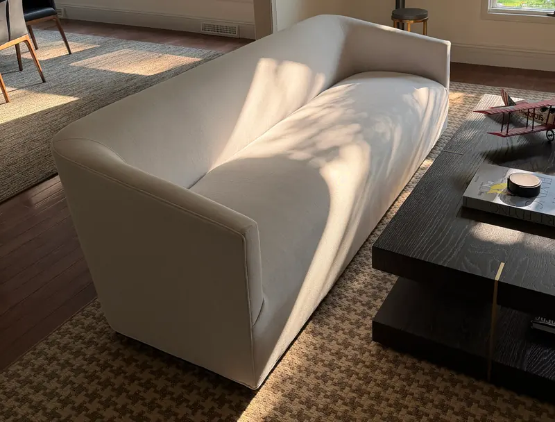 Sofá de lino blanco en una sala soleada, con sombras de hojas sobre el asiento.