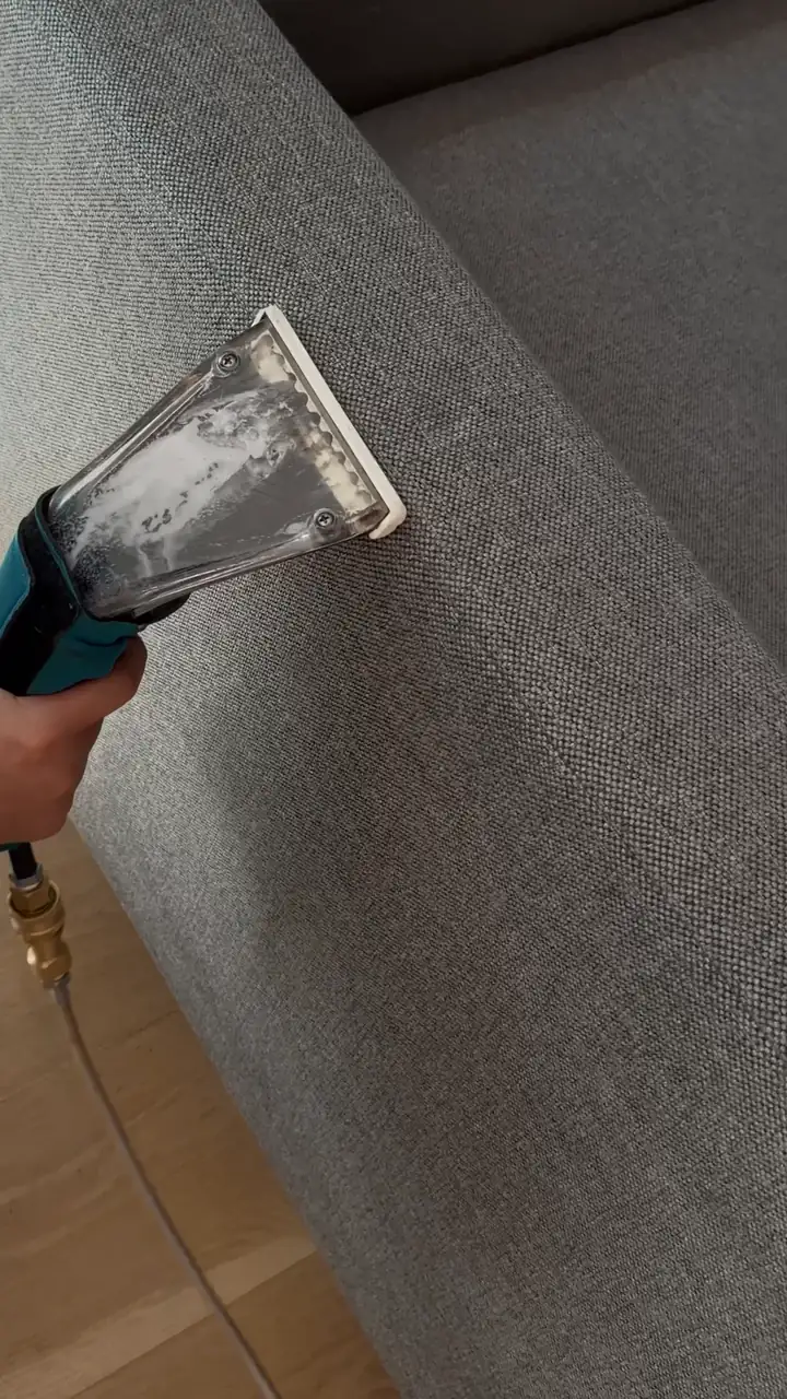 A Pine technician's clear extraction tool on a gray sofa, the head filling with dirty foam